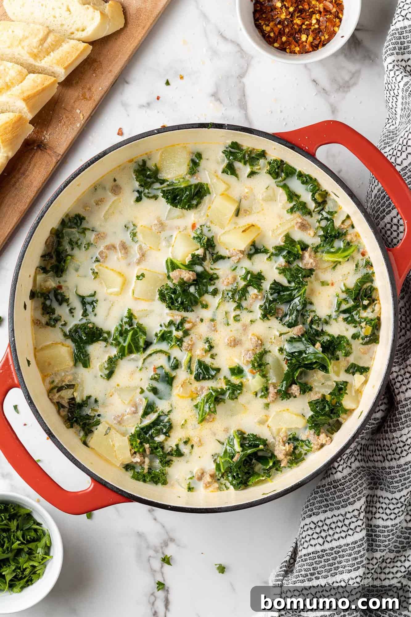 Overhead view of creamy Zuppa Toscana with kale and potatoes in a rustic red Dutch oven, perfectly cooked and ready to serve.