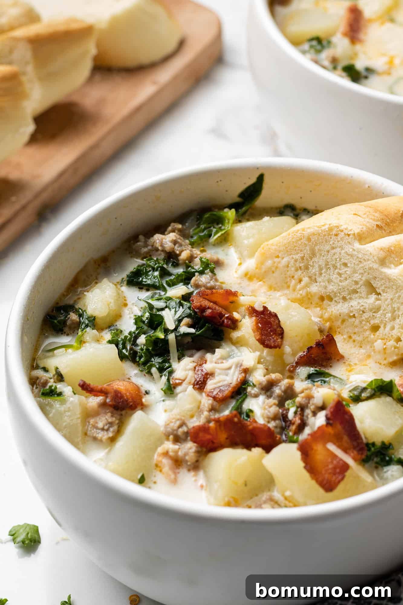 A comforting bowl of Zuppa Toscana in a white bowl, with a piece of crusty bread dipped into the creamy soup, ready to be enjoyed.