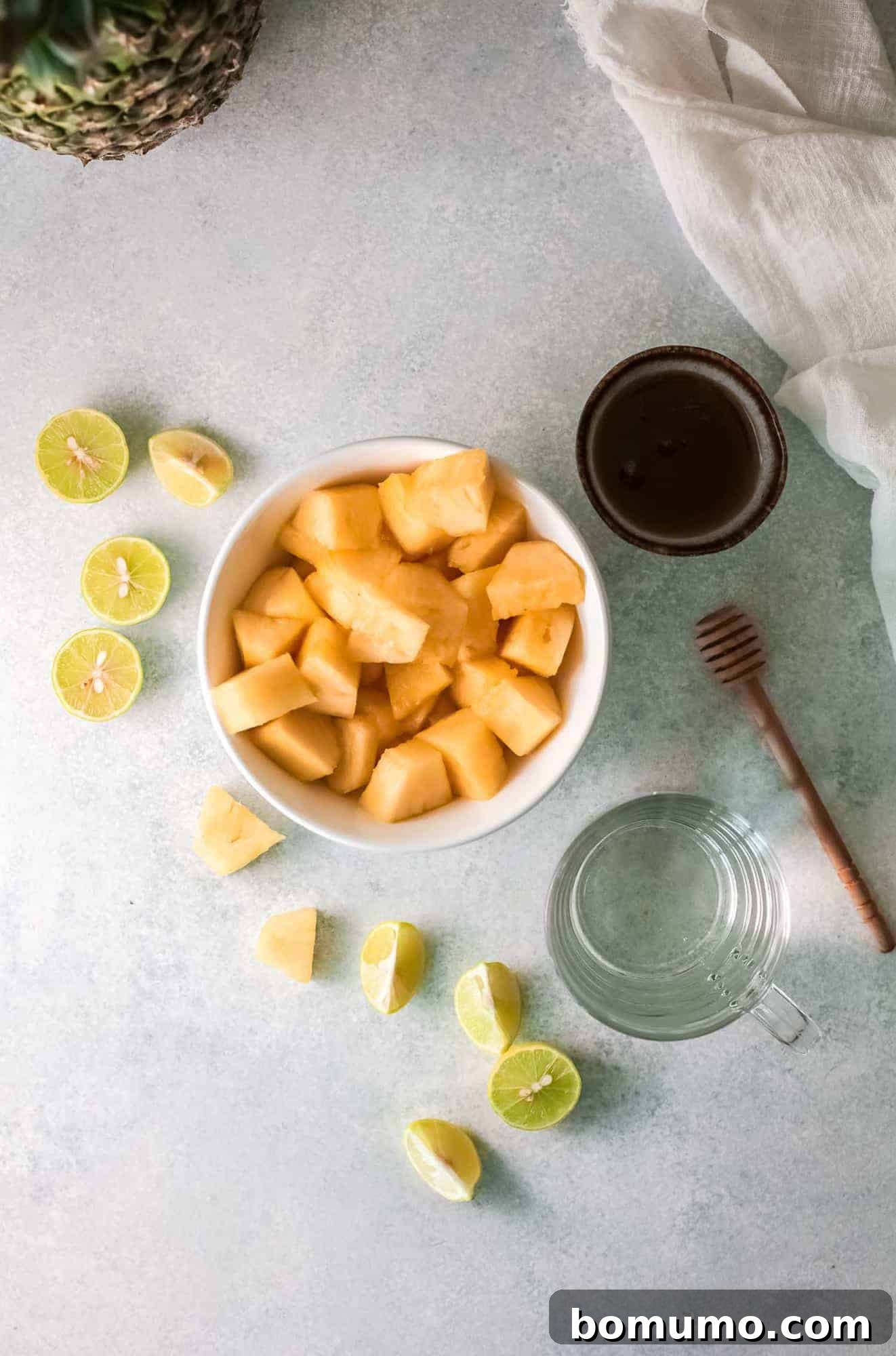 Pineapple Agua Fresca 3 Pineapple, lime, water, and honey laid out on a light grey surface, showcasing the simple ingredients.