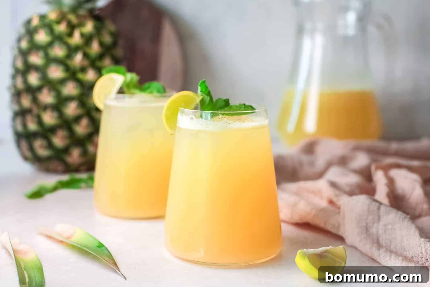 Pineapple Agua Fresca 7 Two glasses of light yellow pineapple water, garnished with fresh mint and lime slices, invitingly presented.