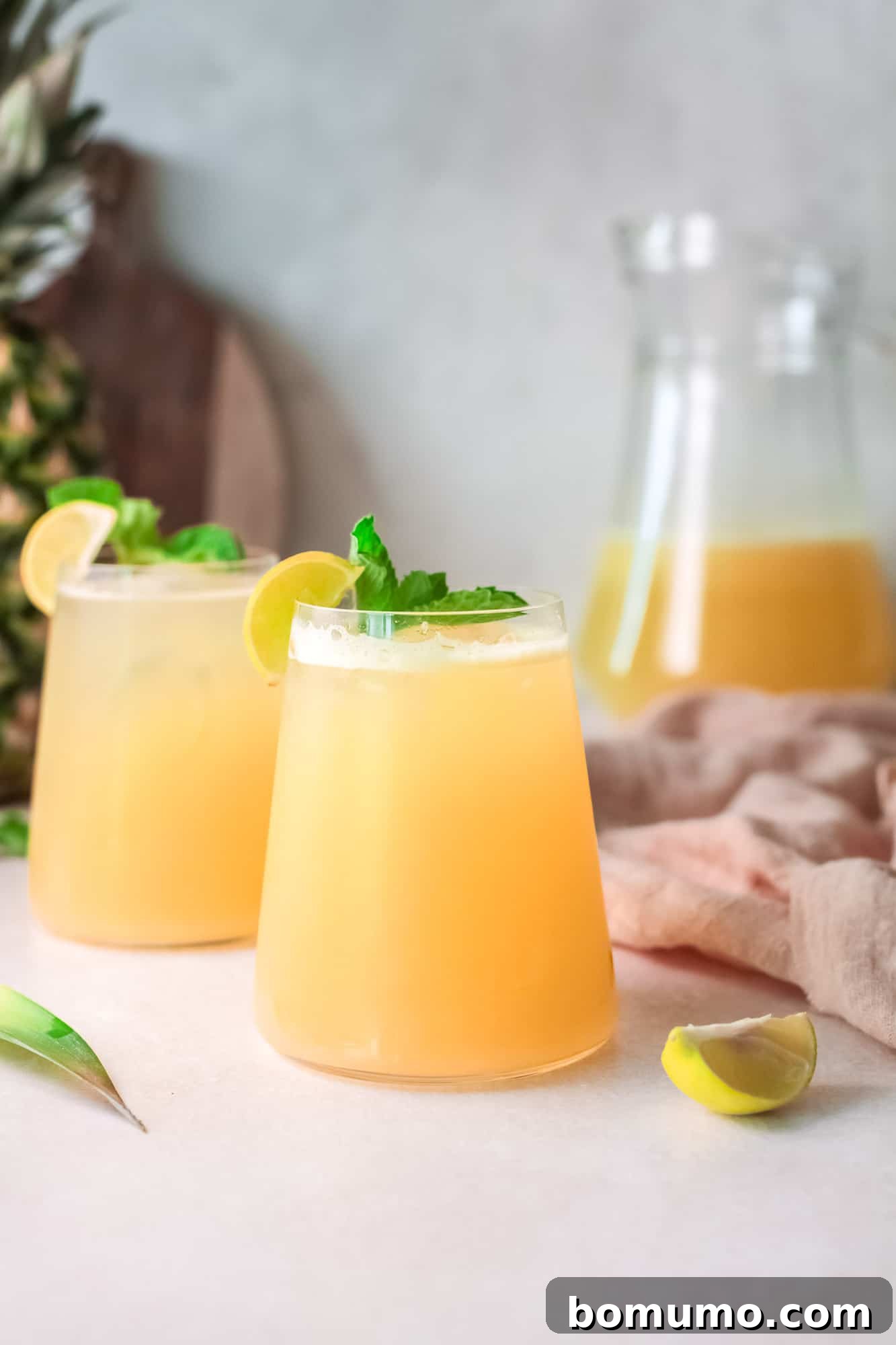 Pineapple Agua Fresca 8 Two glasses filled with a light yellowish-orange beverage, garnished with vibrant fresh mint sprigs, highlighting the drink's refreshing appeal.