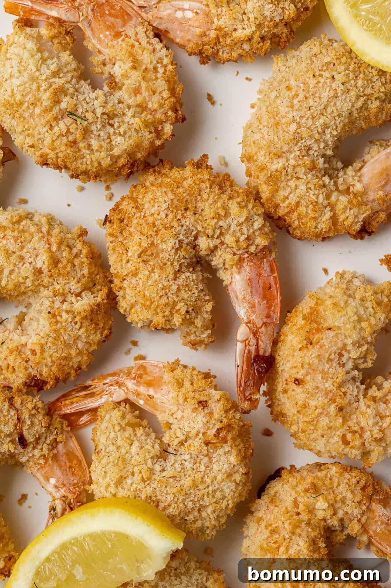 Perfectly golden-brown air fryer breaded shrimp arranged neatly with fresh lemon slices, ready to be enjoyed.