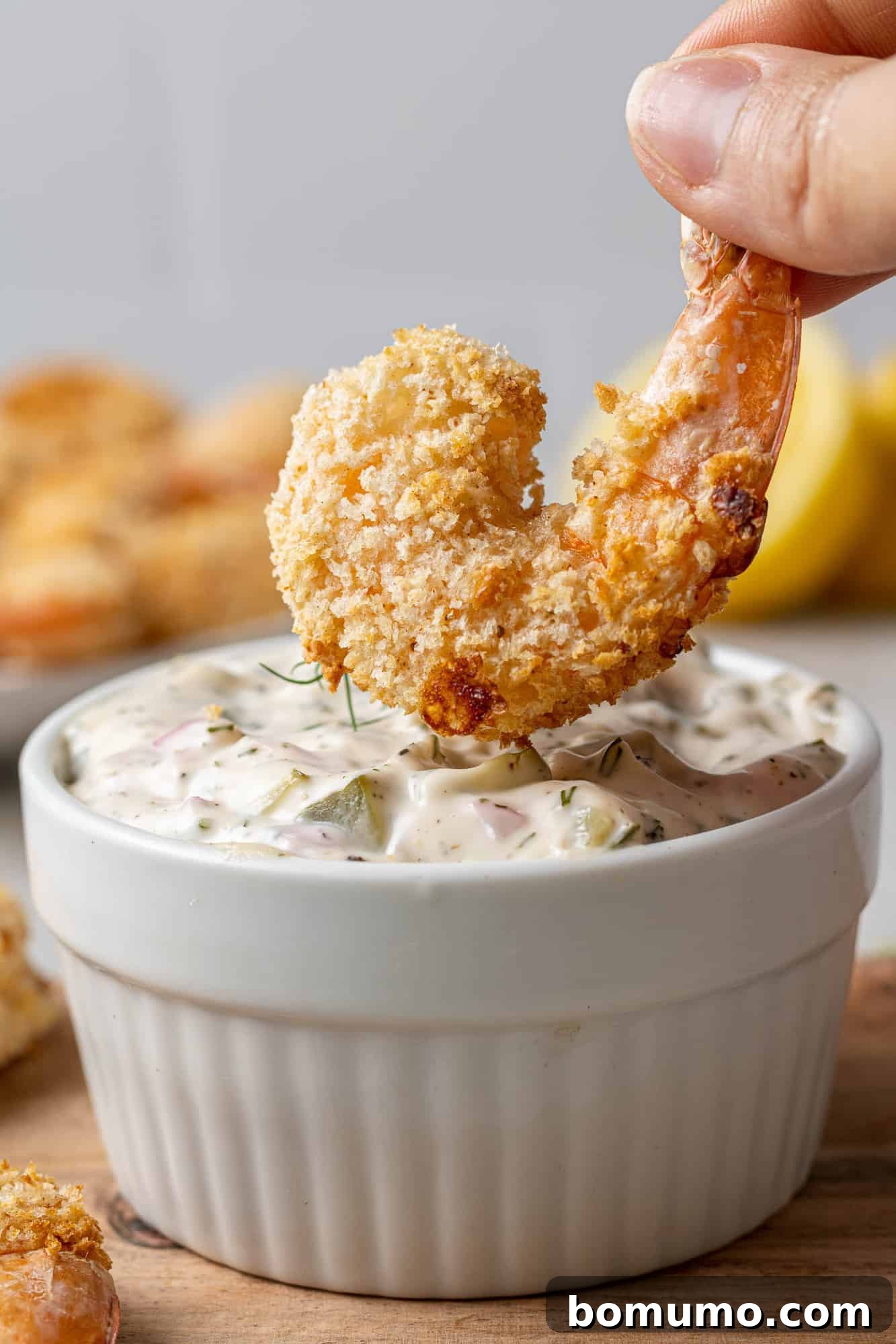 A single piece of perfectly breaded air fryer shrimp being dipped into a creamy, vibrant tartar sauce, ready for a delicious bite.