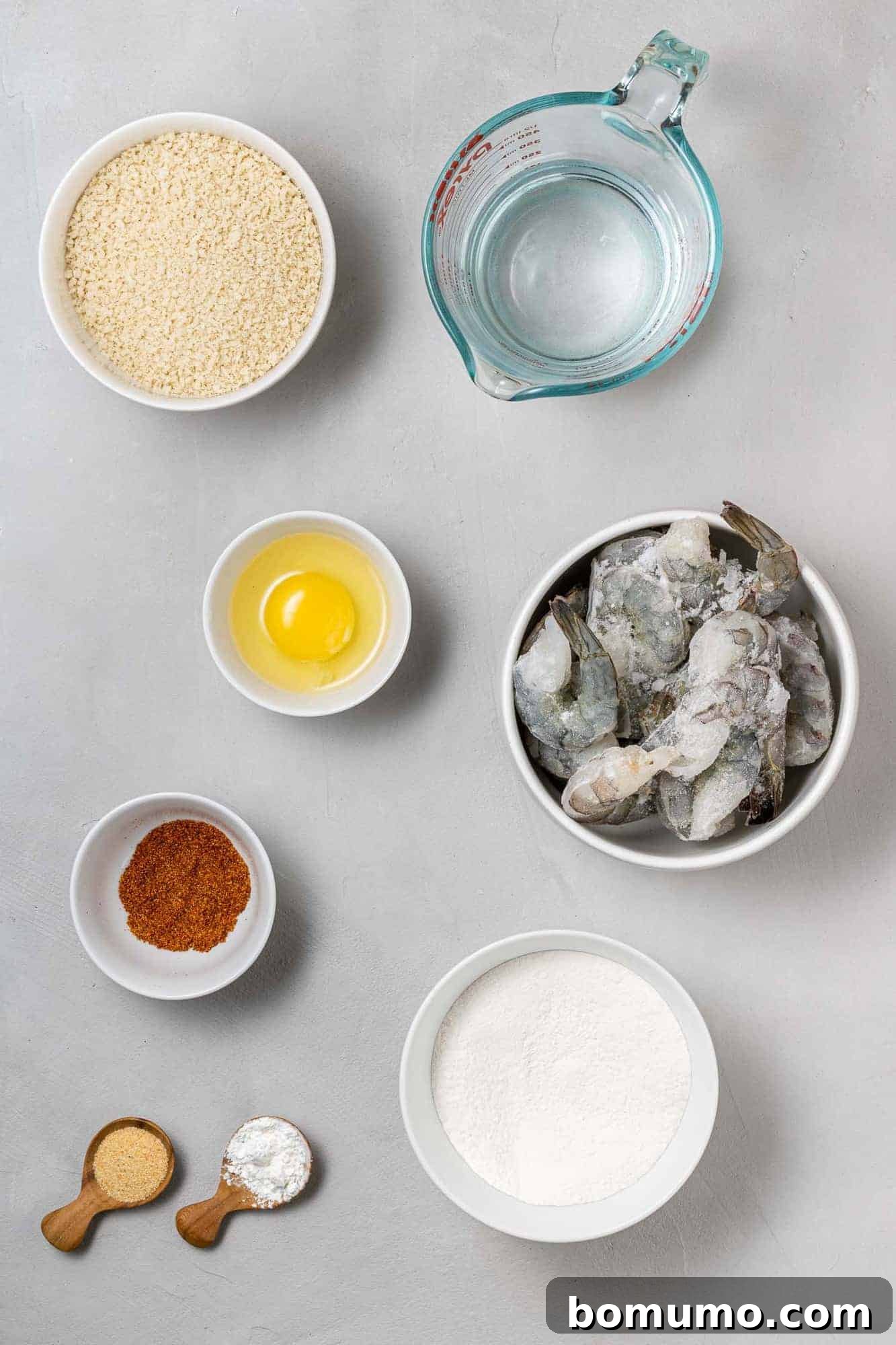 An overhead shot showcasing all the fresh and essential ingredients laid out for making air fryer breaded shrimp, including raw shrimp, panko, flour, eggs, and seasonings.