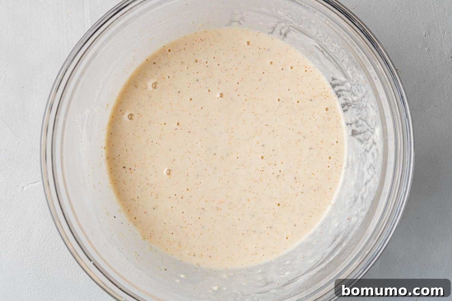 Close-up of a smooth, golden batter mixture in a clear glass mixing bowl, ready for coating the shrimp.