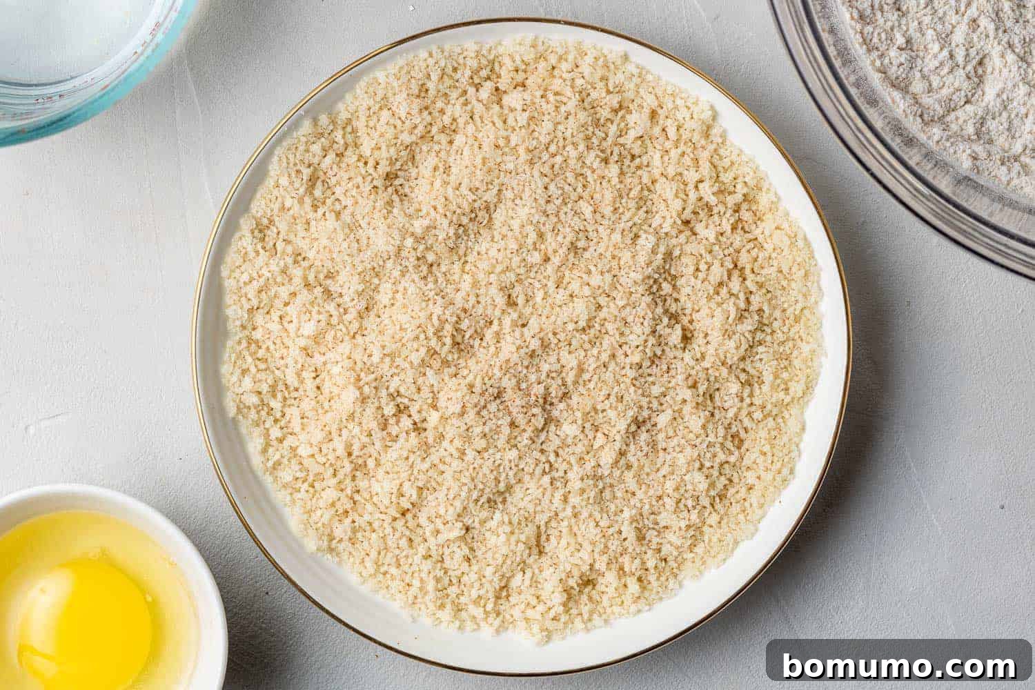 Close-up of light and airy Panko bread crumbs seasoned with Old Bay, sitting in a clear glass mixing bowl, forming the second coating station.