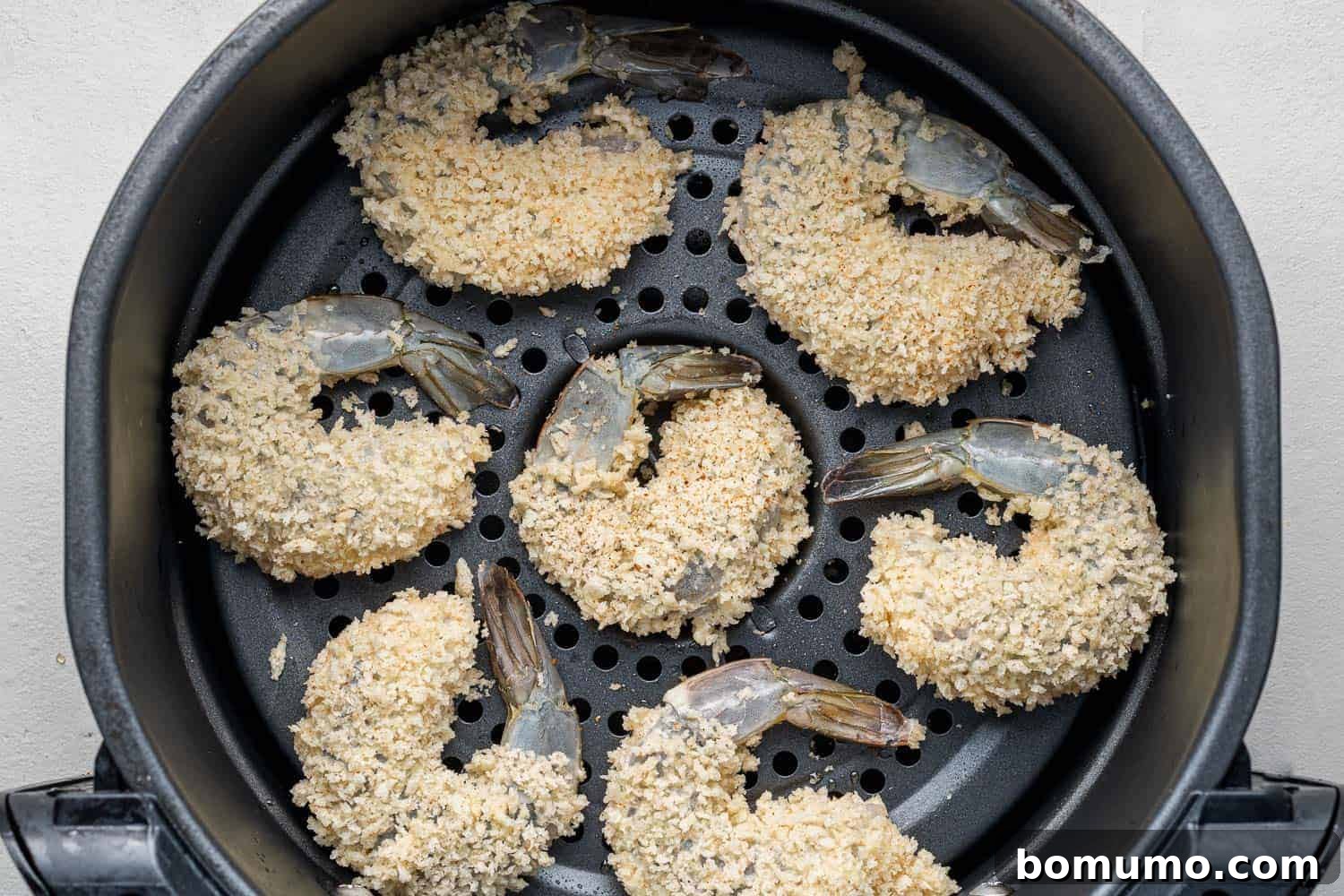Uncooked, breaded shrimp neatly arranged in a single layer within an air fryer basket, ready for cooking.