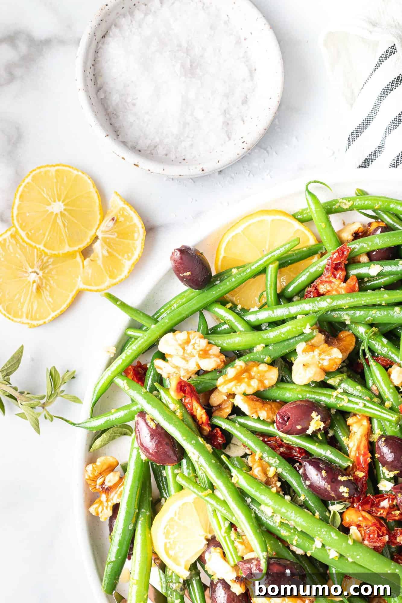 Colorful green bean salad, lemon slices and salt nearby.