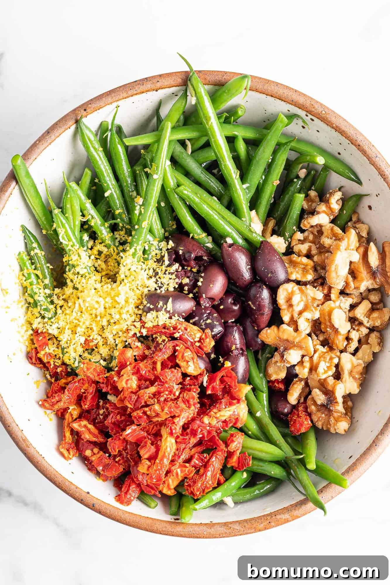Green bean salad, not yet mixed. Lemon zest, sun dried tomatoes, kalamatas, and walnuts in piles on top of green beans.
