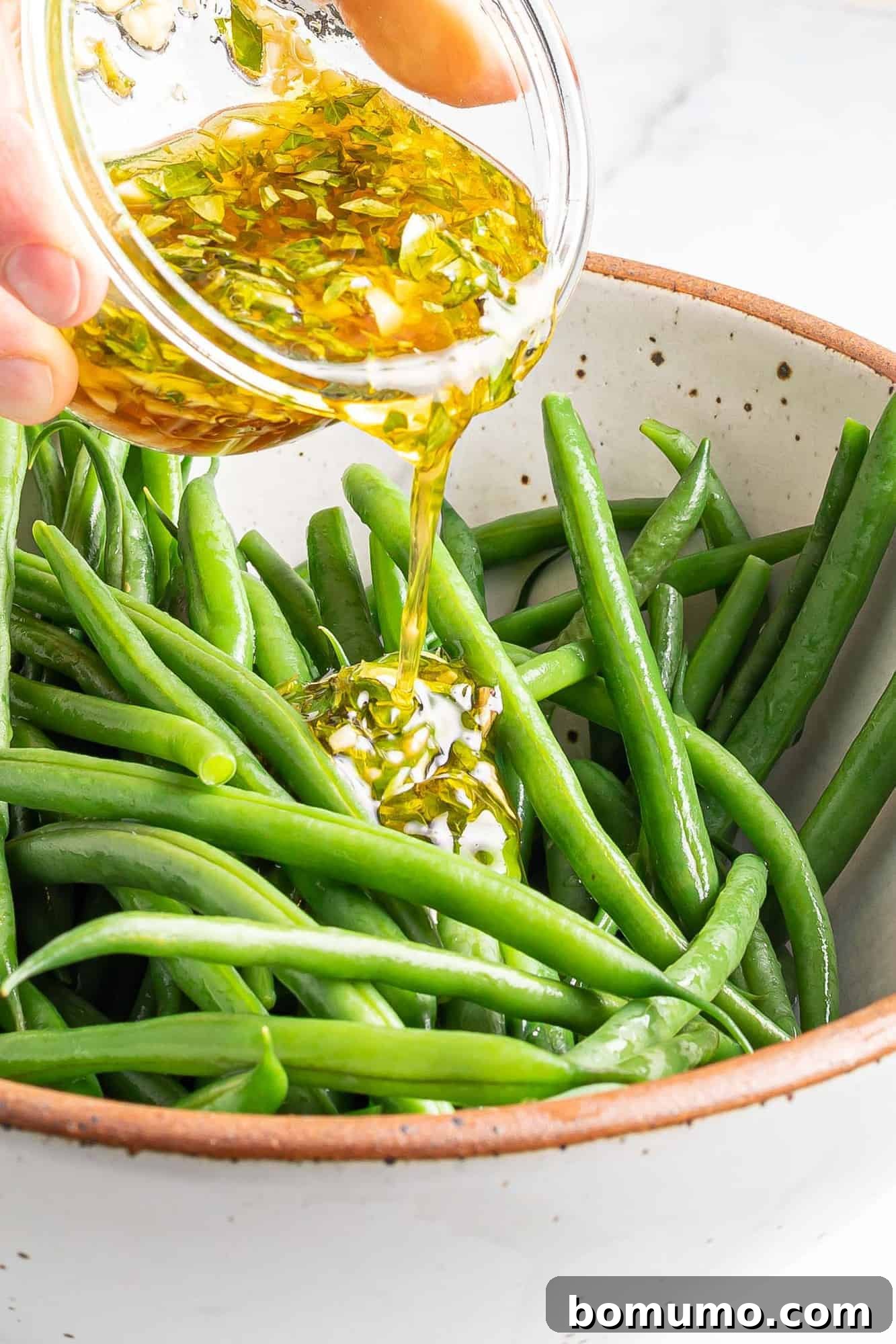 Dressing being poured on green beans.
