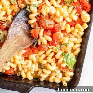 Pasta with feta and tomatoes, served in a black baking dish with a wooden spoon for stirring.