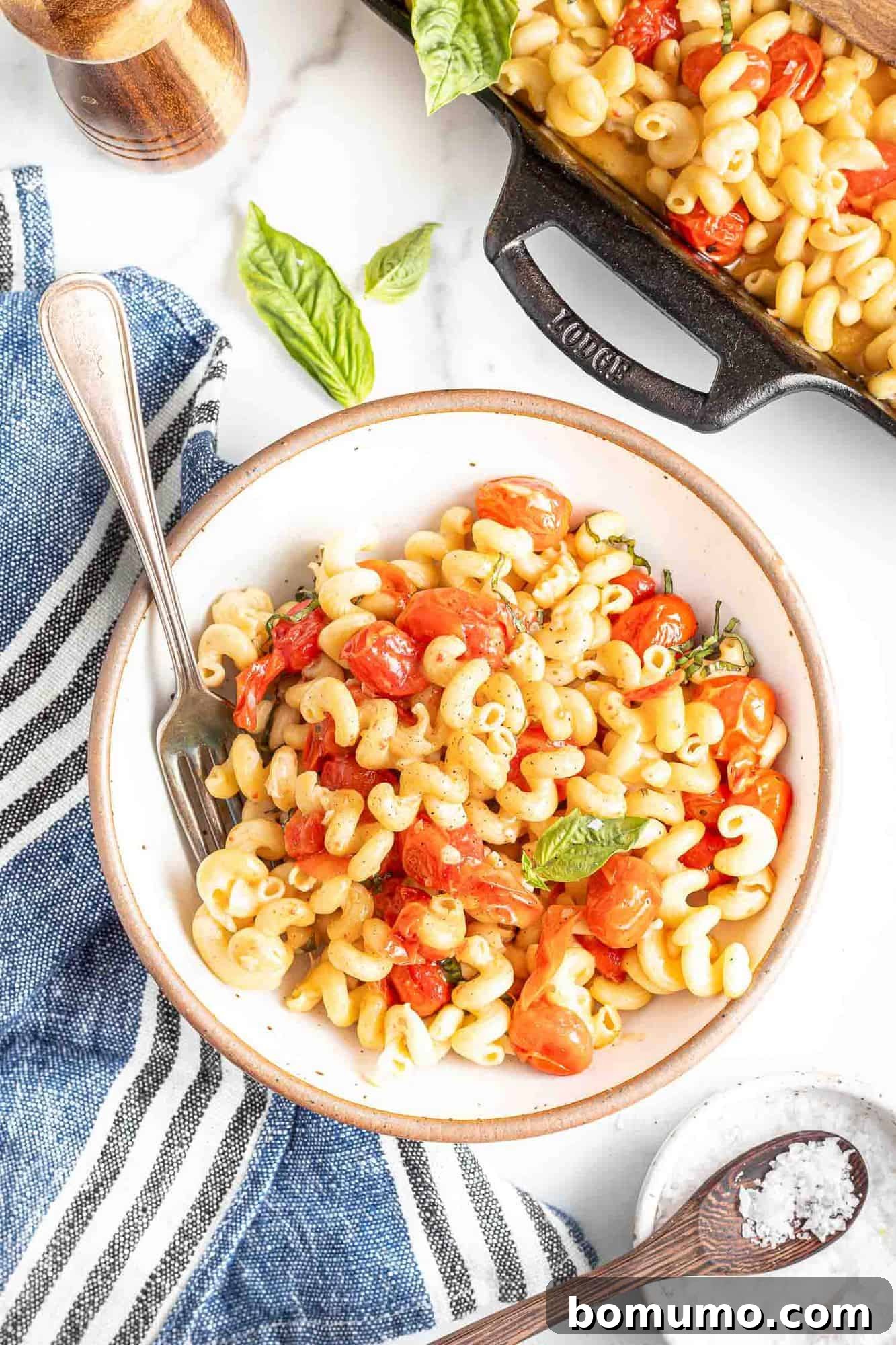 A vibrant bowl of baked feta pasta, adorned with roasted tomatoes and a generous sprinkle of fresh basil, ready to be enjoyed.