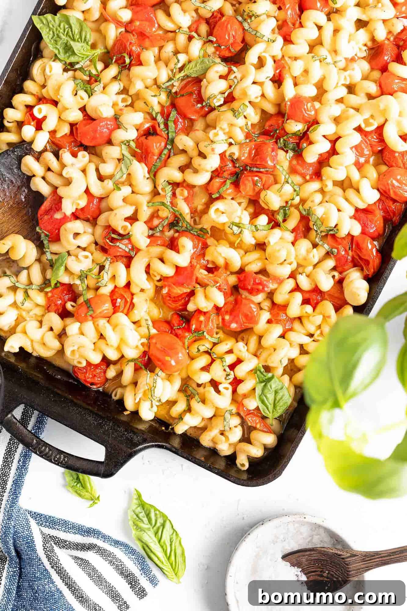 A black baking dish brimming with rich baked feta pasta, adorned with roasted tomatoes and a generous sprinkle of fresh basil, ready for serving.
