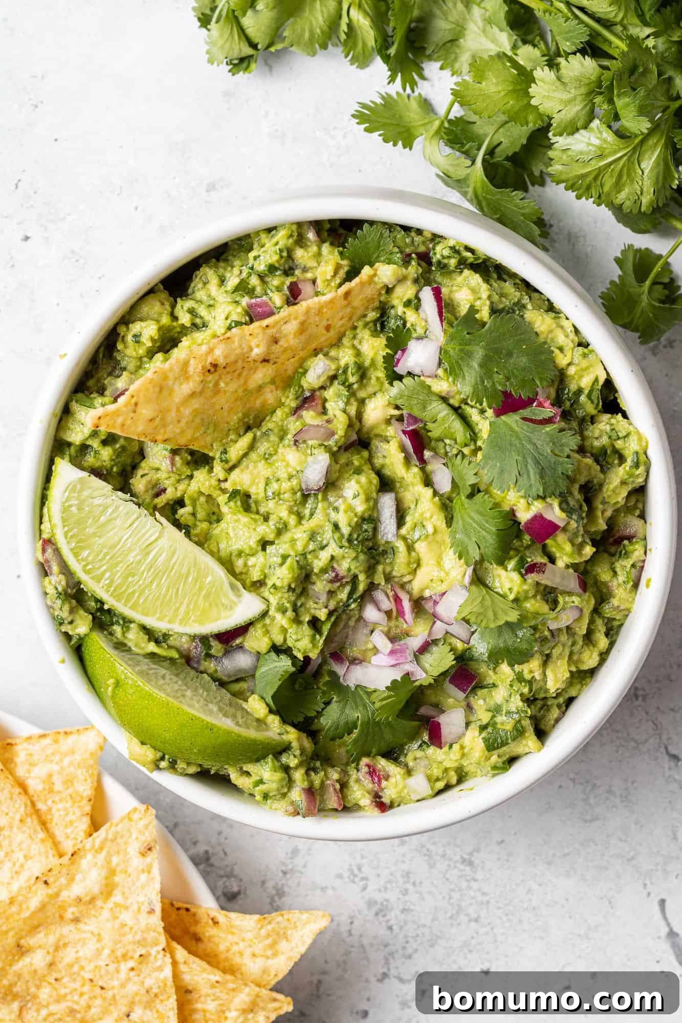 Crafting Perfect Guacamole 12 Overhead view of a pristine white bowl of guacamole, garnished with lime wedges and a chip, symbolizing freshness.