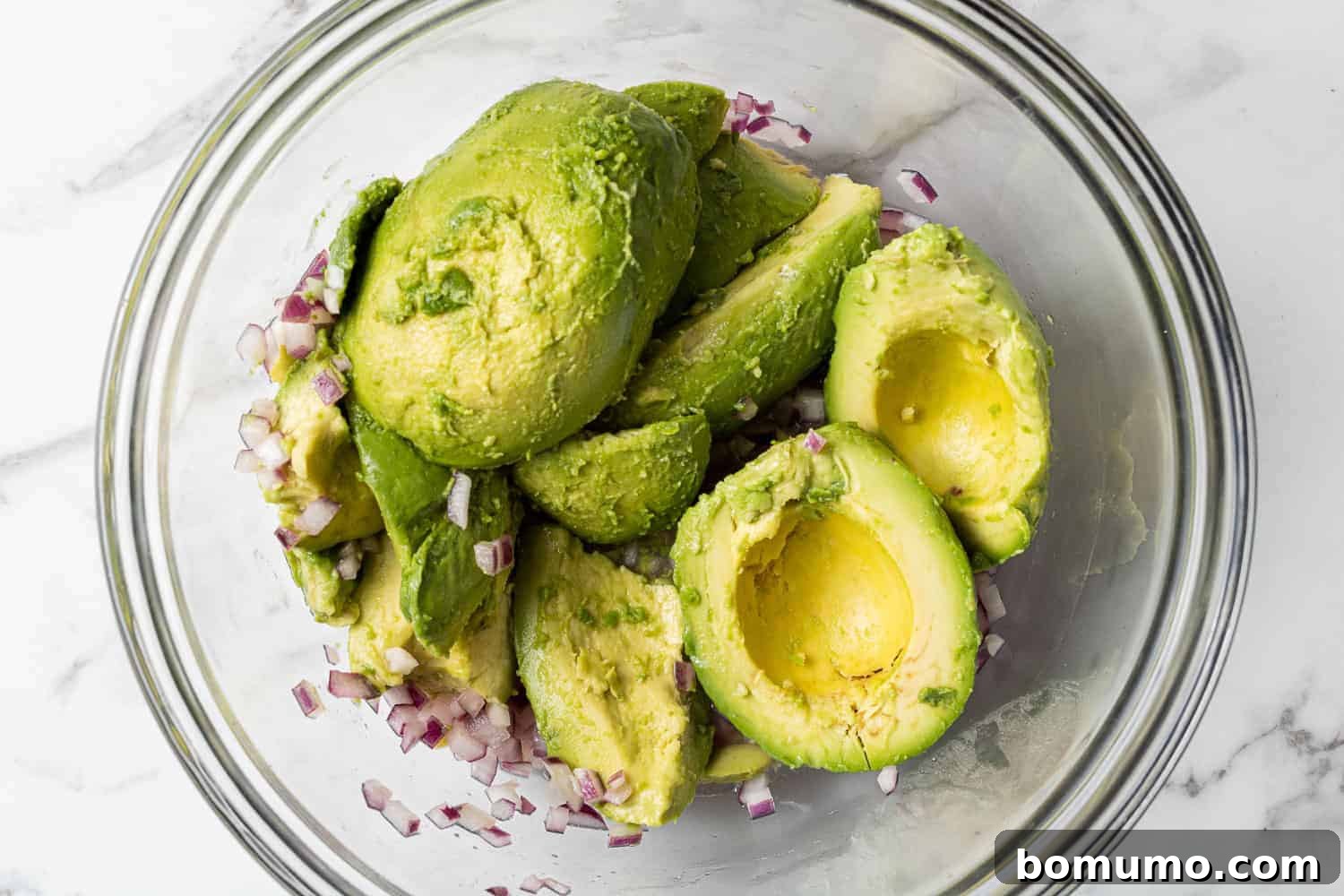 Crafting Perfect Guacamole 6 Peeled avocado halves, ready for mashing, resting in a bowl alongside softened red onions.