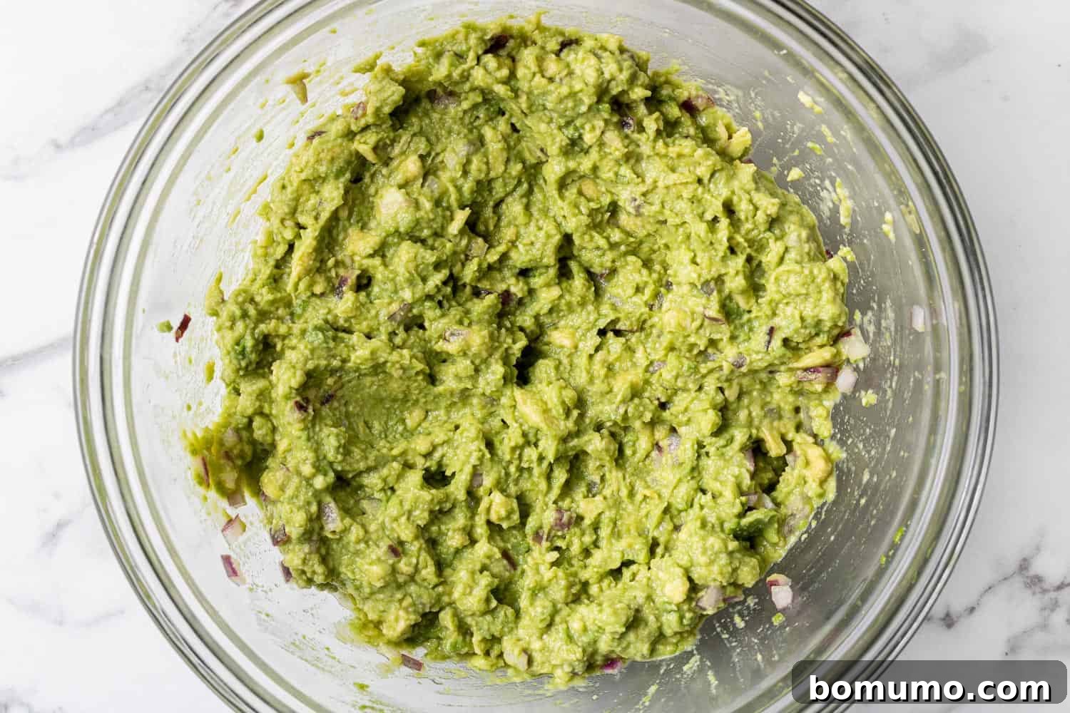 Crafting Perfect Guacamole 7 Mashed avocado in a clear glass bowl, showcasing the desired creamy yet slightly chunky texture.