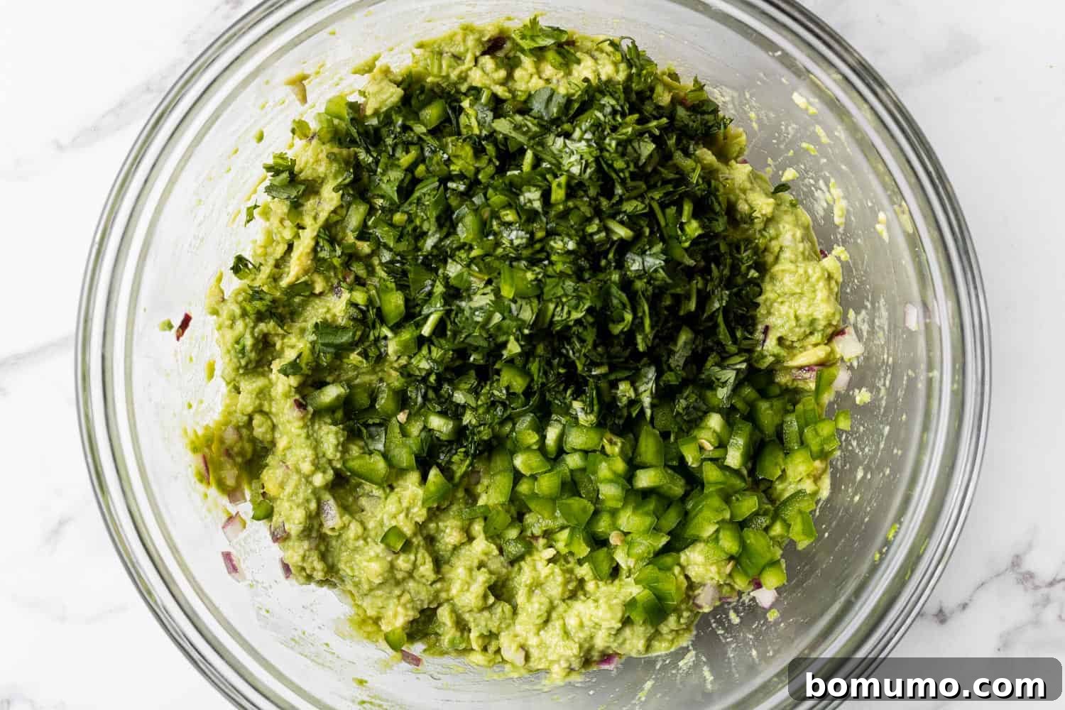 Crafting Perfect Guacamole 8 Finely diced jalapeño and fresh cilantro resting atop mashed avocado, ready to be mixed in.