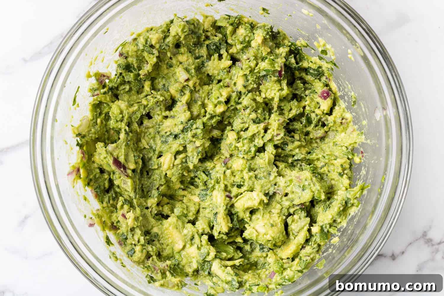 Crafting Perfect Guacamole 9 A vibrant bowl of freshly prepared guacamole in a clear glass mixing bowl, showcasing its rich green color.