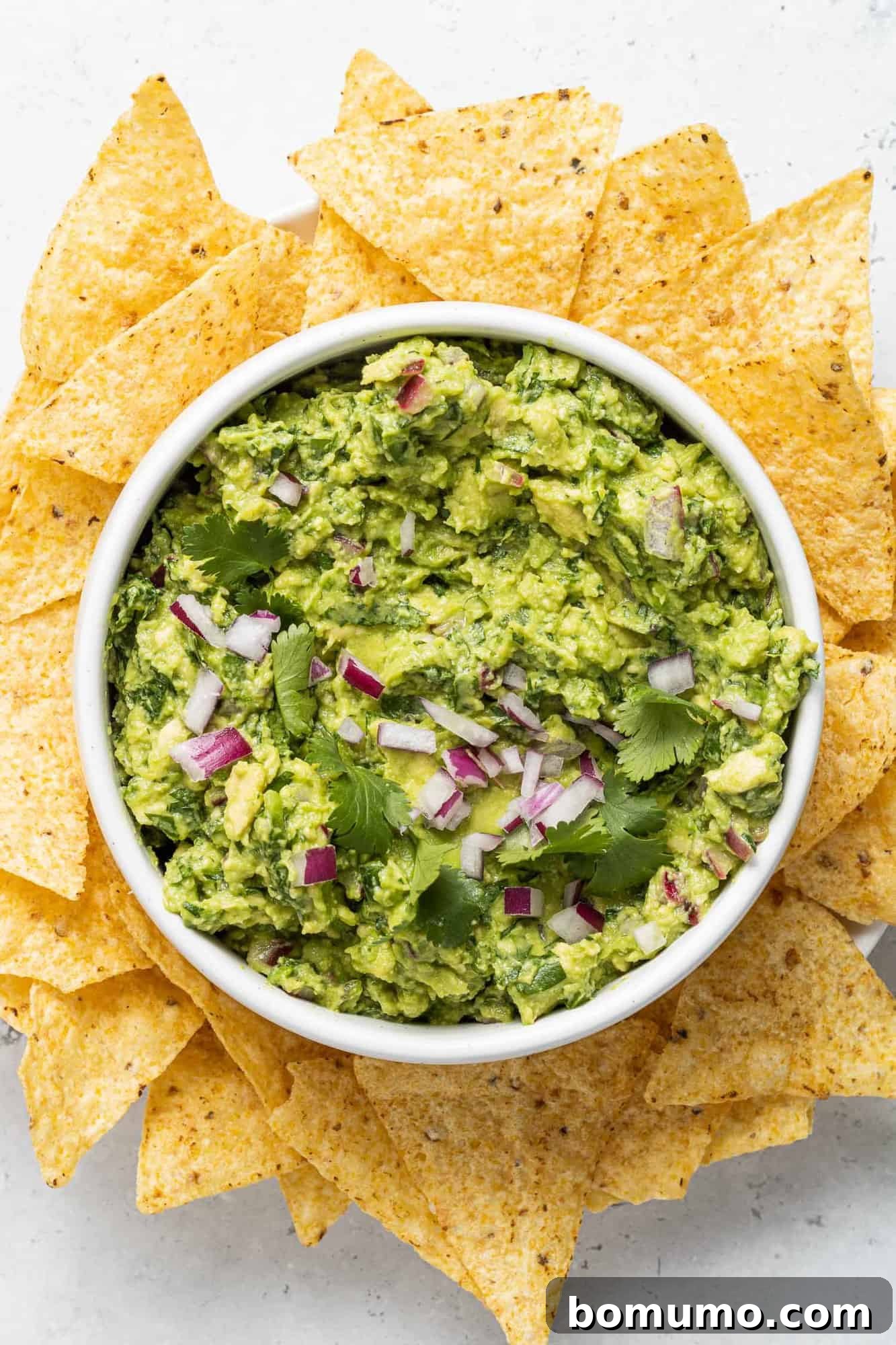 Crafting Perfect Guacamole 10 A beautifully presented bowl of guacamole, garnished with lime wedges and a single chip dipped in, surrounded by more chips.