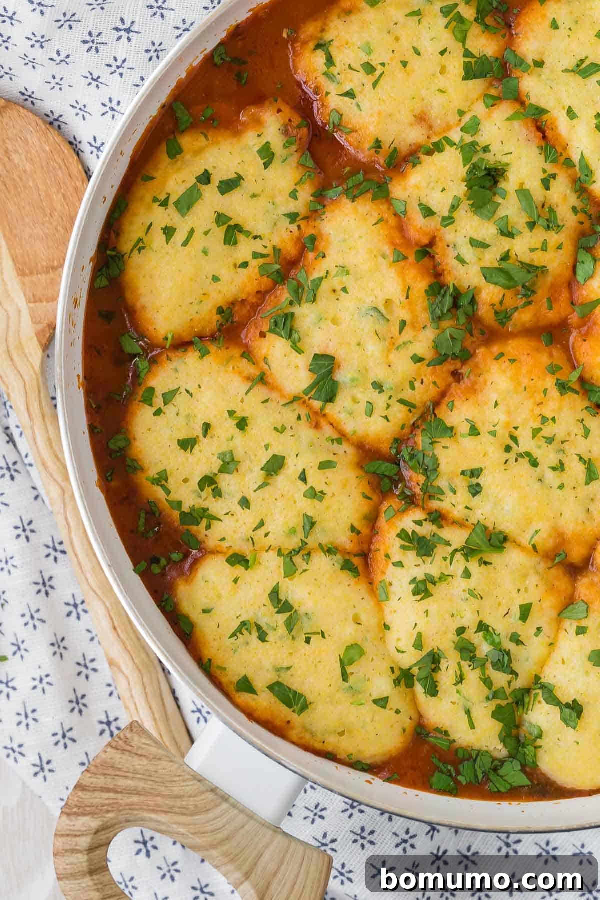 Hearty cornmeal dumplings simmering in a vibrant tomato broth within a white pot.