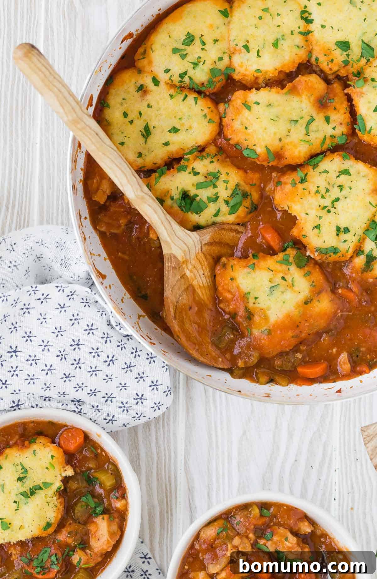 A pan filled with savory tomato sauce, tender chicken, and fluffy cornmeal biscuits.