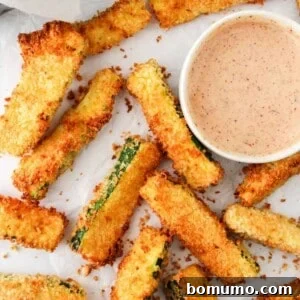Air fryer zucchini fries on parchment with a light red dipping sauce.