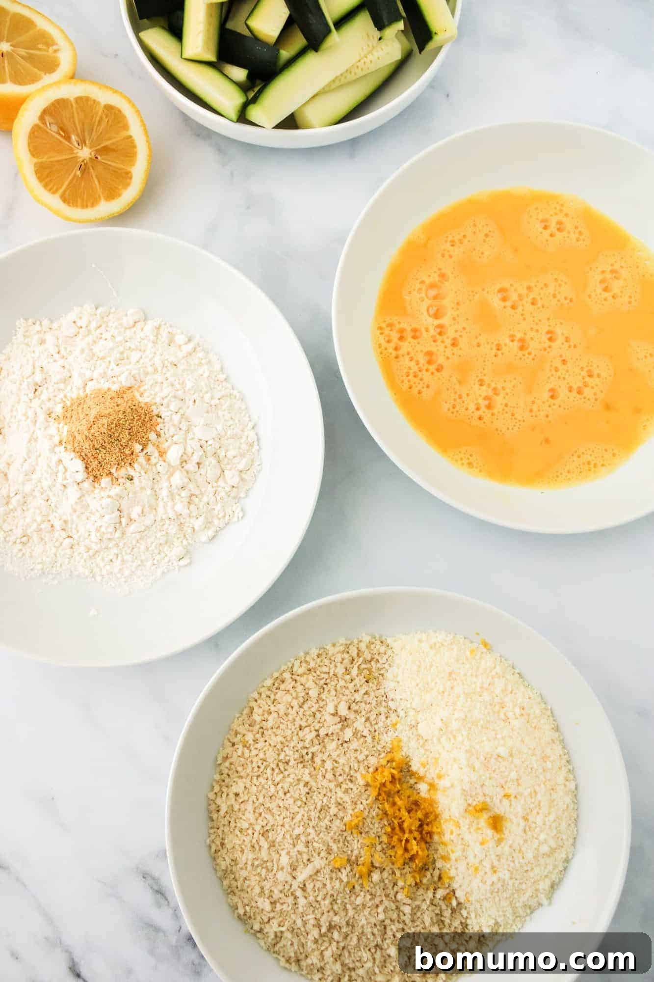 Three shallow bowls demonstrating the breading stages: seasoned flour, beaten eggs, and the panko-Parmesan mixture.
