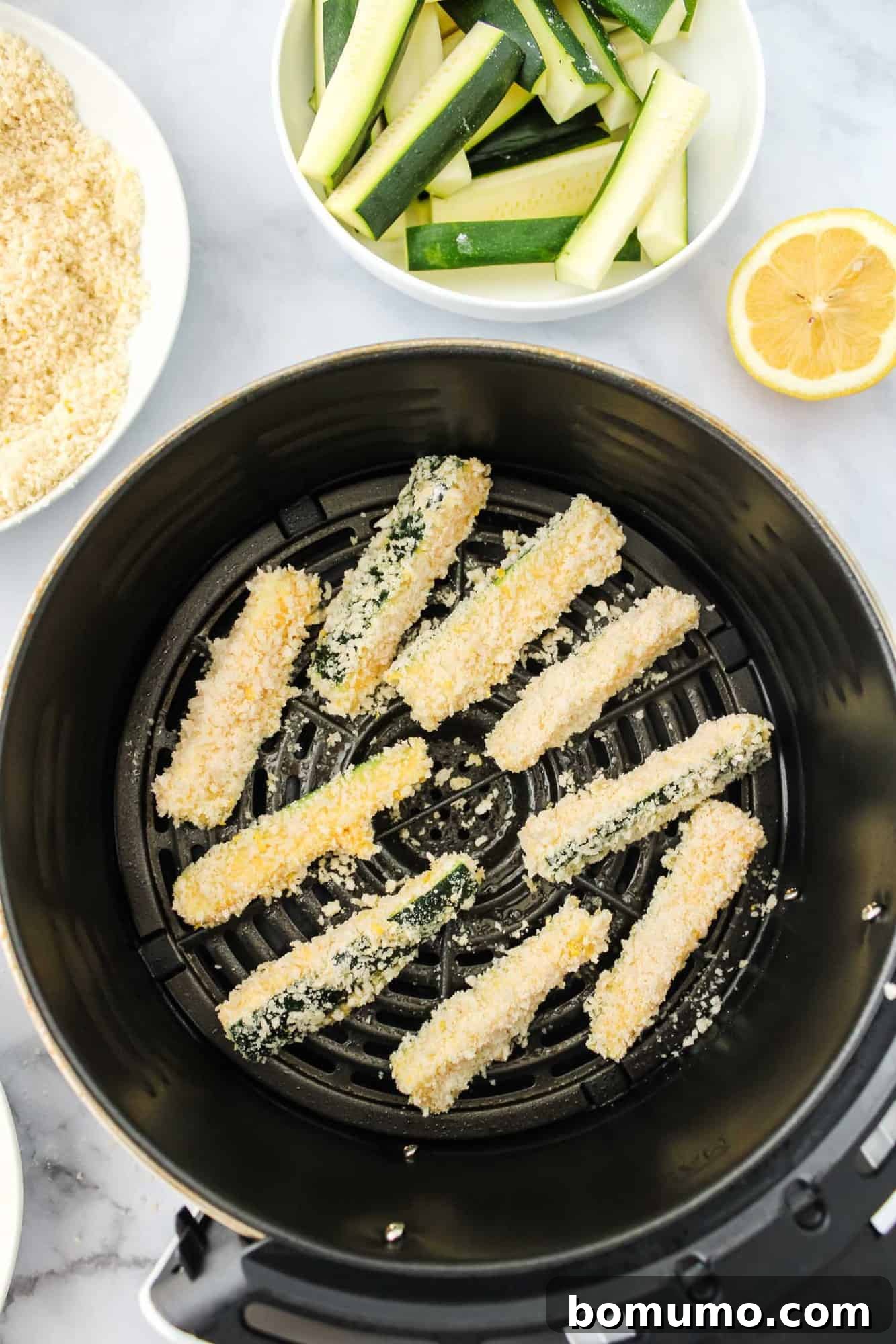 Uncooked, breaded zucchini fries neatly arranged in an air fryer basket, ready for cooking.