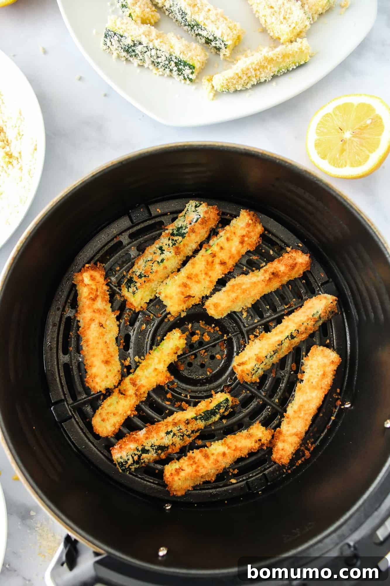 Freshly cooked, golden-brown zucchini fries filling an air fryer basket.