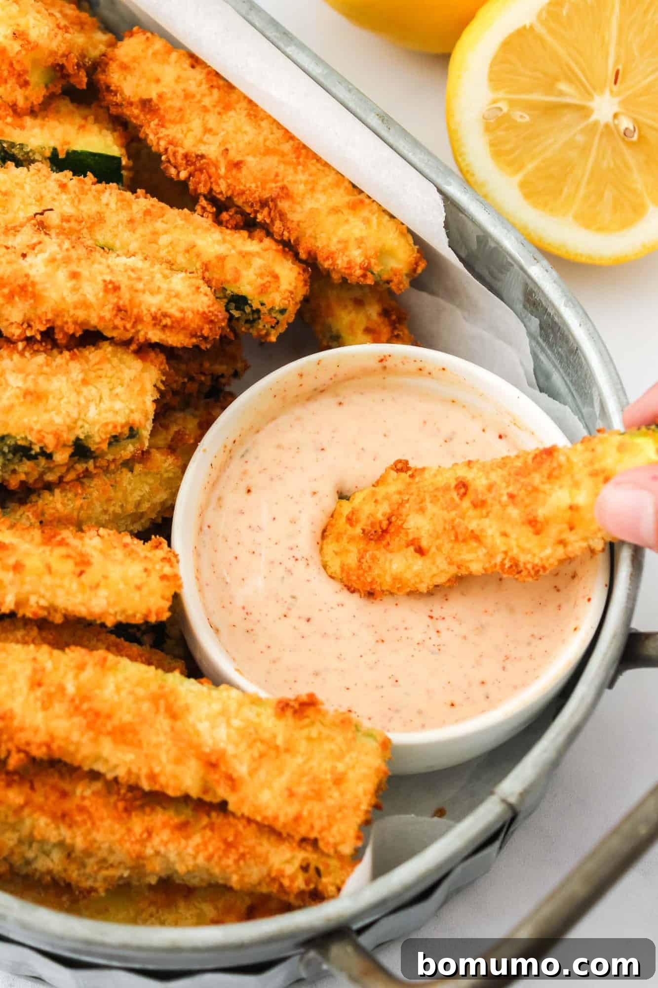 A crispy zucchini fry being dipped into a swirl of light red chili ranch sauce.