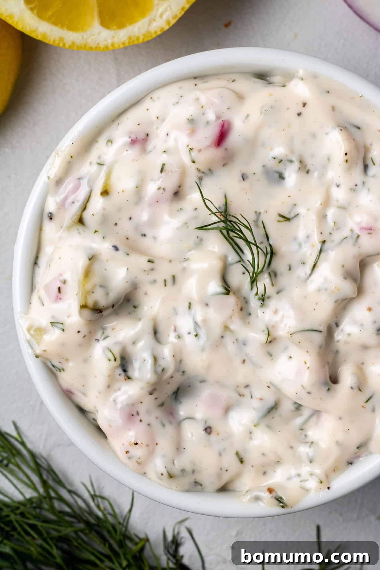 Overhead view of homemade tartar sauce in a round white bowl garnished with fresh dill, ready to be served.