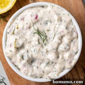 Overhead view of tartar sauce in a round white bowl garnished with fresh dill.