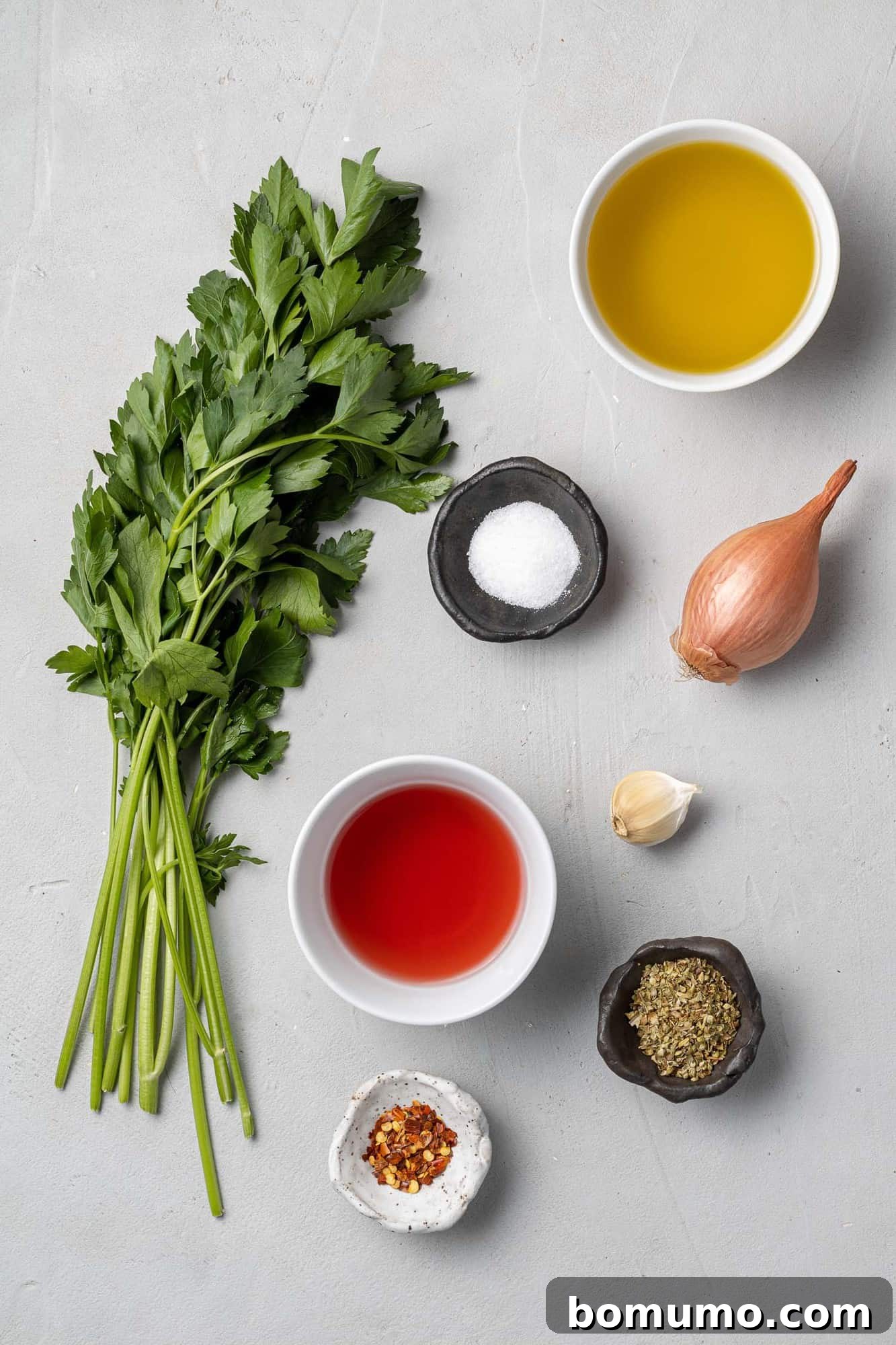 A flat lay view showcasing all the fresh ingredients meticulously arranged for the chimichurri recipe, including parsley, garlic, olive oil, and red pepper flakes.