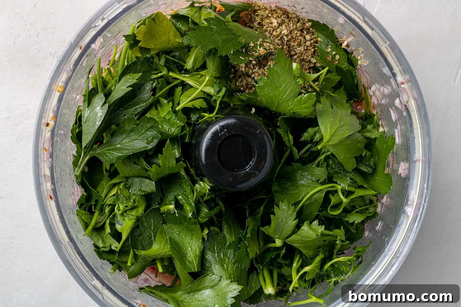A vibrant pile of fresh parsley leaves loaded into a food processor bowl, ready to be blended into chimichurri.