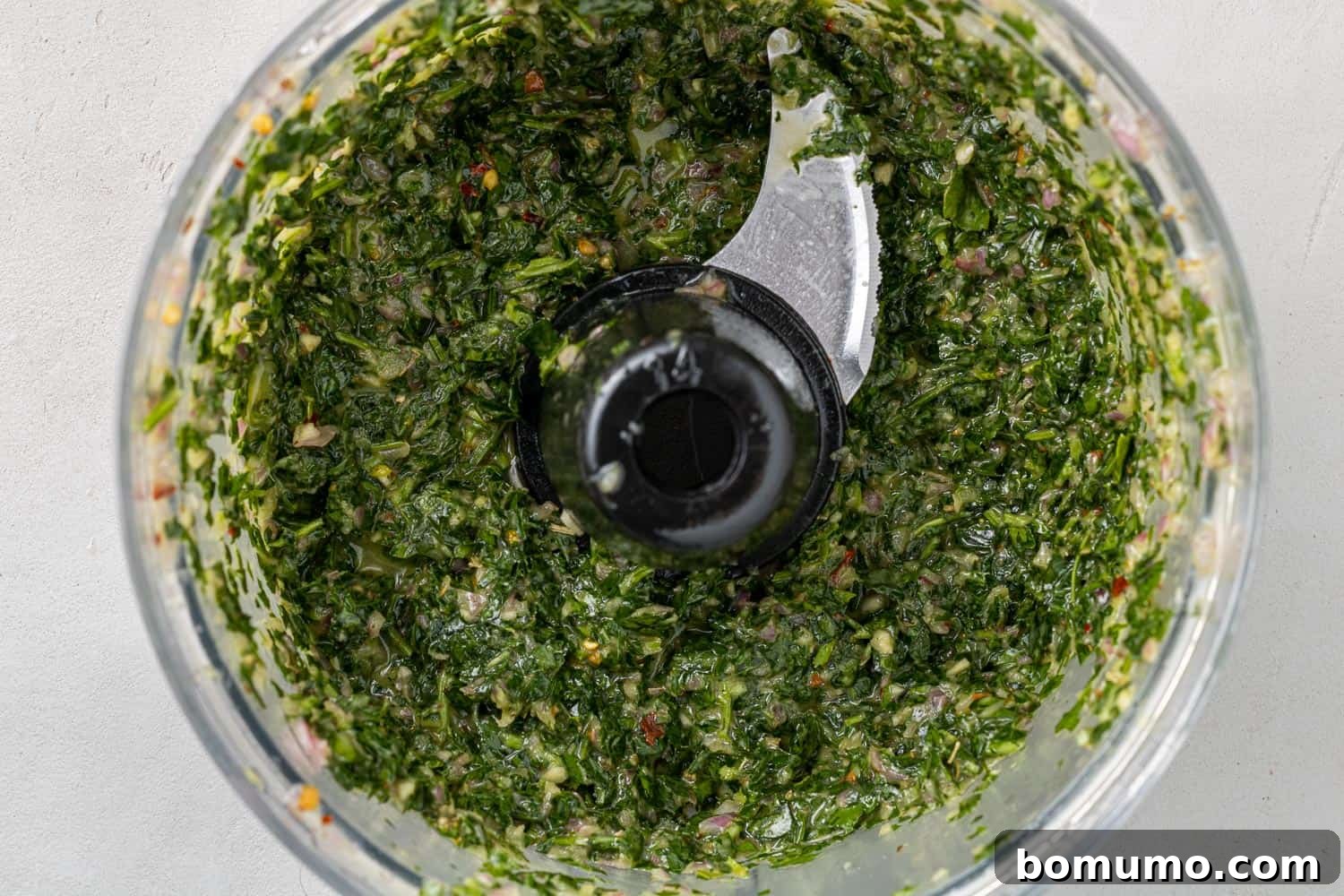 Freshly pulsed chimichurri sauce in a food processor, showing its vibrant green color and chunky texture.