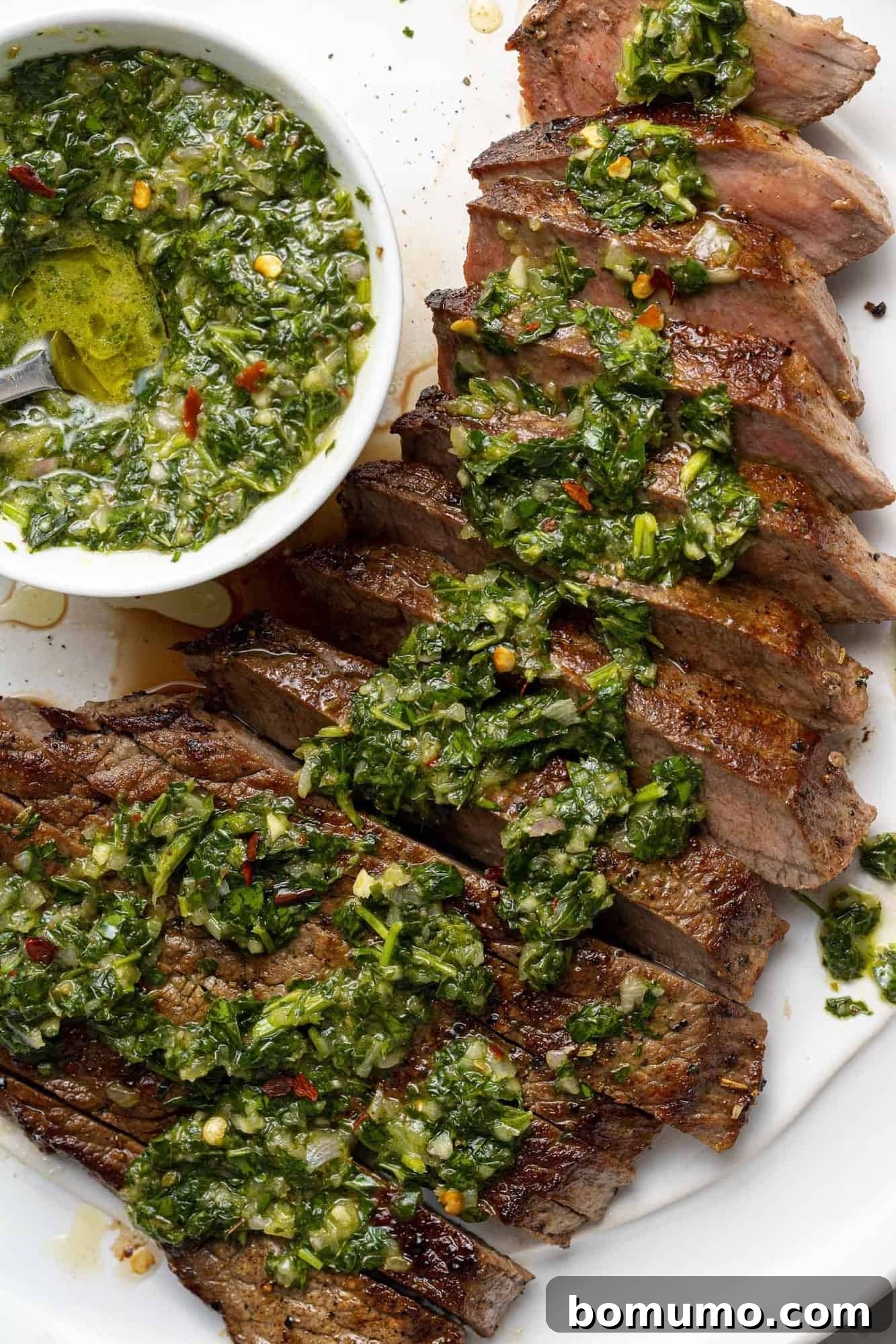 A close-up of perfectly cooked sliced steak, generously topped with vibrant green chimichurri sauce, illustrating a classic serving suggestion.