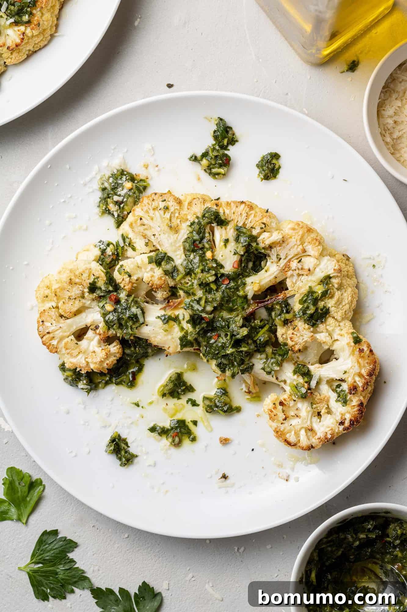 A thick slice of roasted cauliflower, generously topped with vibrant green chimichurri sauce, highlighting its meaty texture.