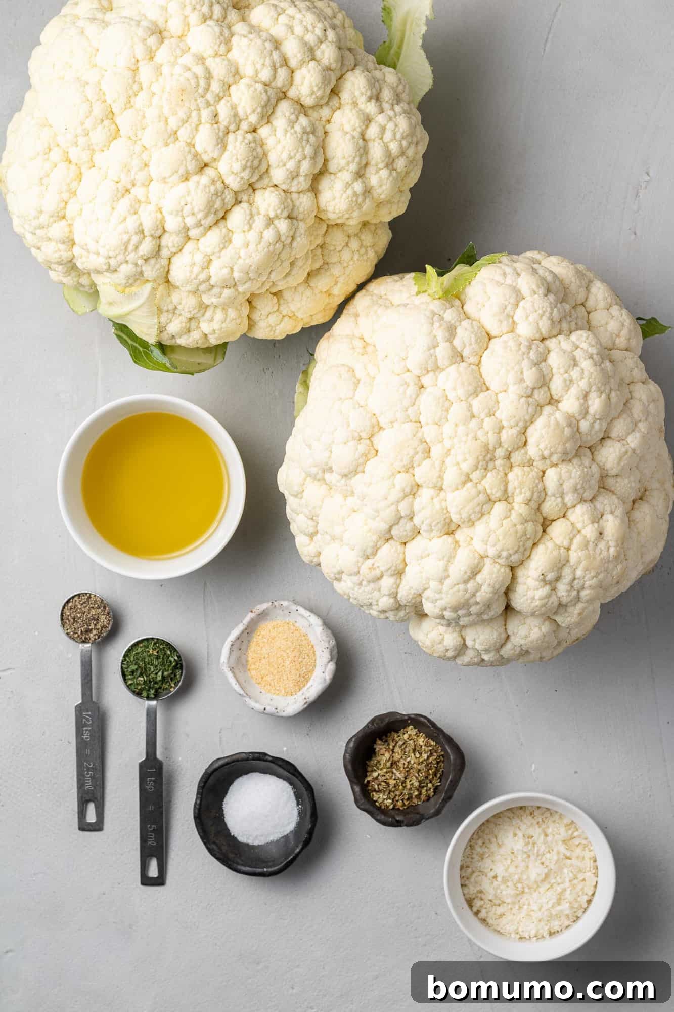 An overhead view of all the fresh ingredients needed for the cauliflower steak recipe, including two pristine heads of cauliflower.