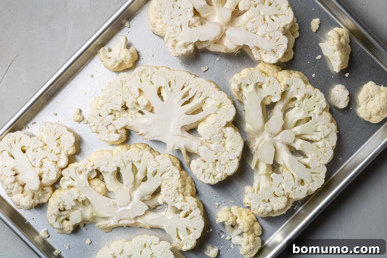 Neatly arranged cauliflower slices on a silver sheet pan, ready for seasoning.