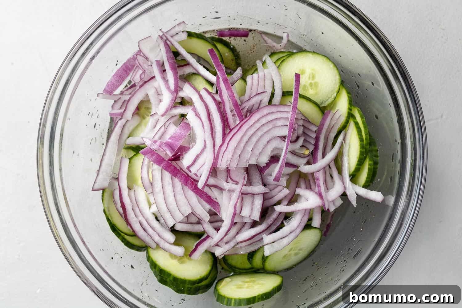 Cucumbers and sliced onions in a large glass mixing bowl.