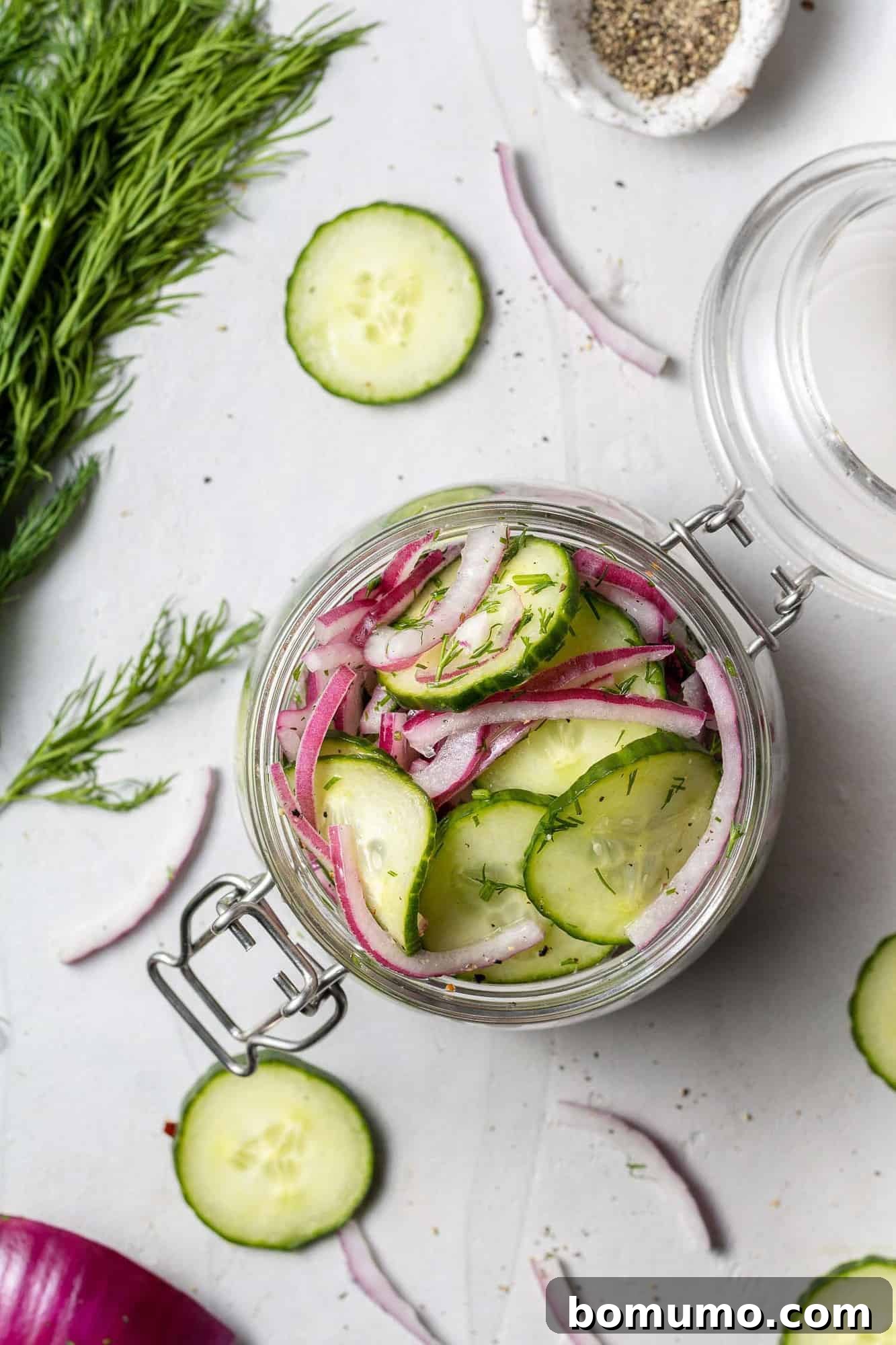 Overhead view of cucumbers and onions in a small glass jar.
