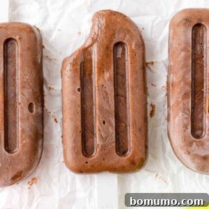 Three chocolate pudding pops, one with a bite removed, showcasing the creamy texture of this easy homemade frozen treat.
