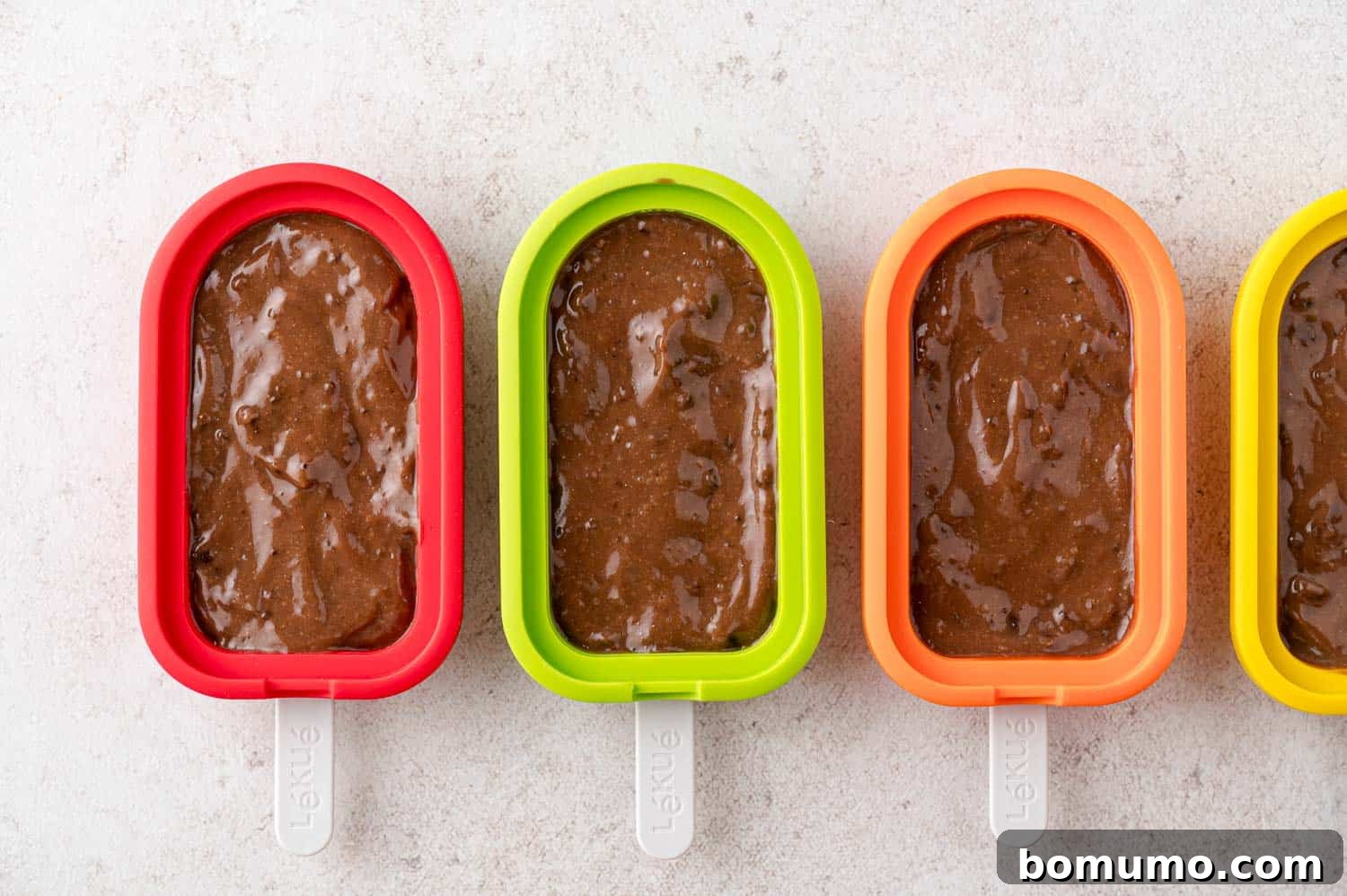 Creamy chocolate pudding mixture being carefully poured into individual popsicle molds.