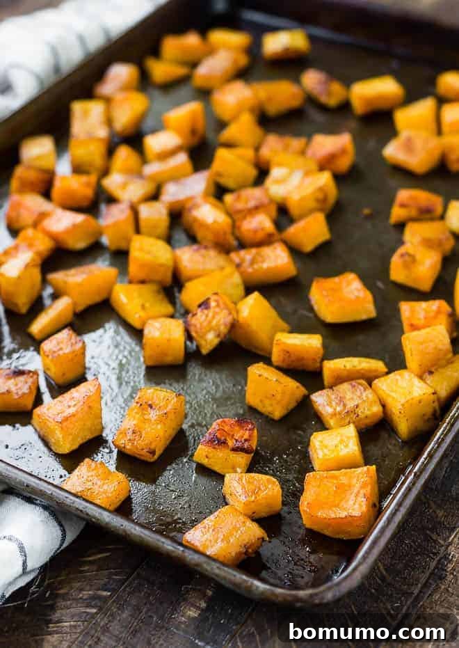 Close-up of vibrant orange roasted butternut squash cubes in a white bowl, seasoned with spices.