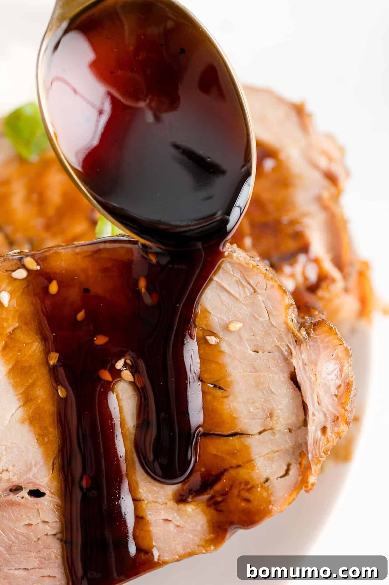 Thick balsamic glaze being poured over succulent pork loin slices.