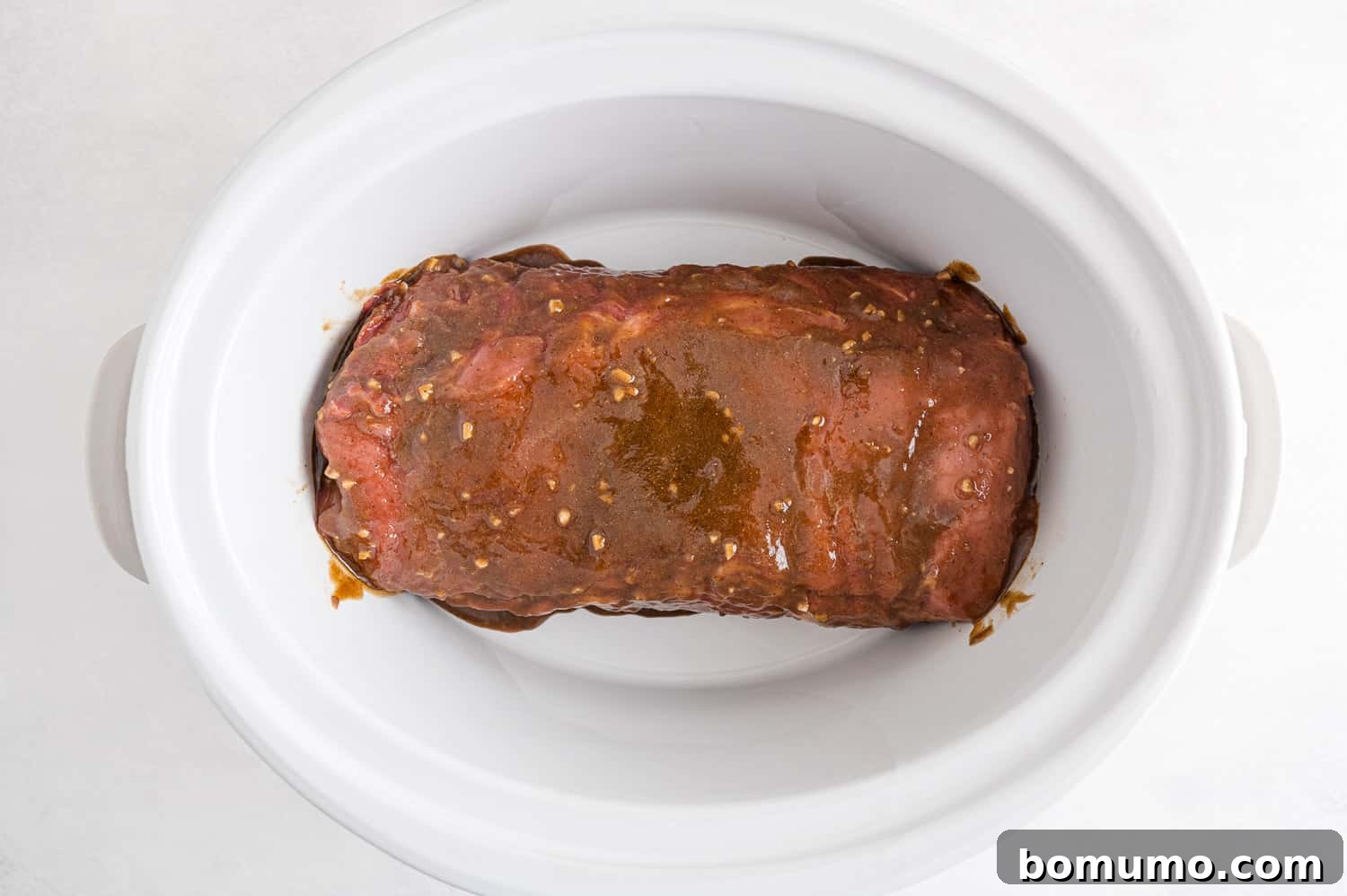 Pork loin cooking in a slow cooker, covered.