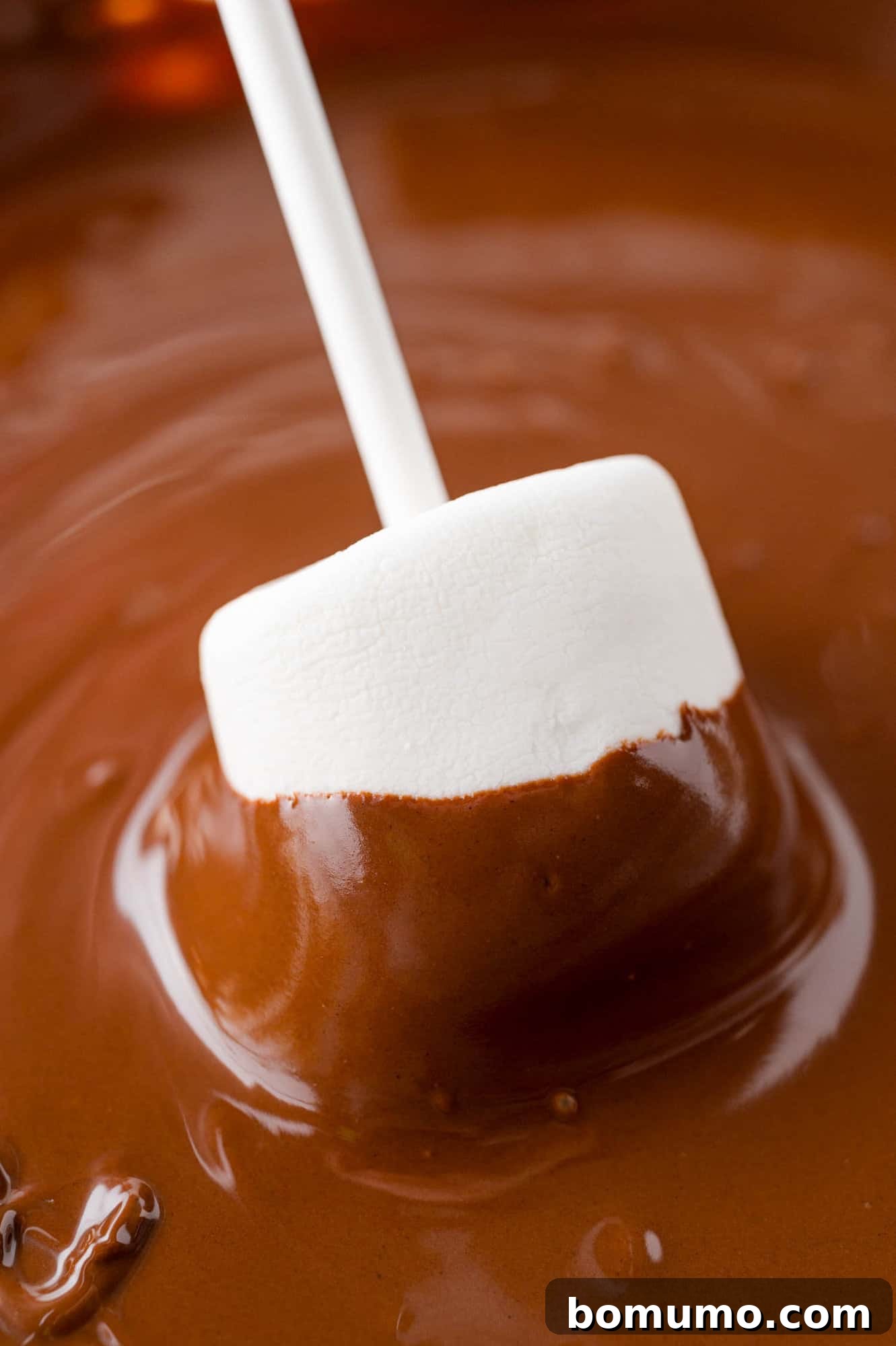 Velvet Dipped Mallows 10 A marshmallow being carefully dipped into a bowl of melted chocolate.