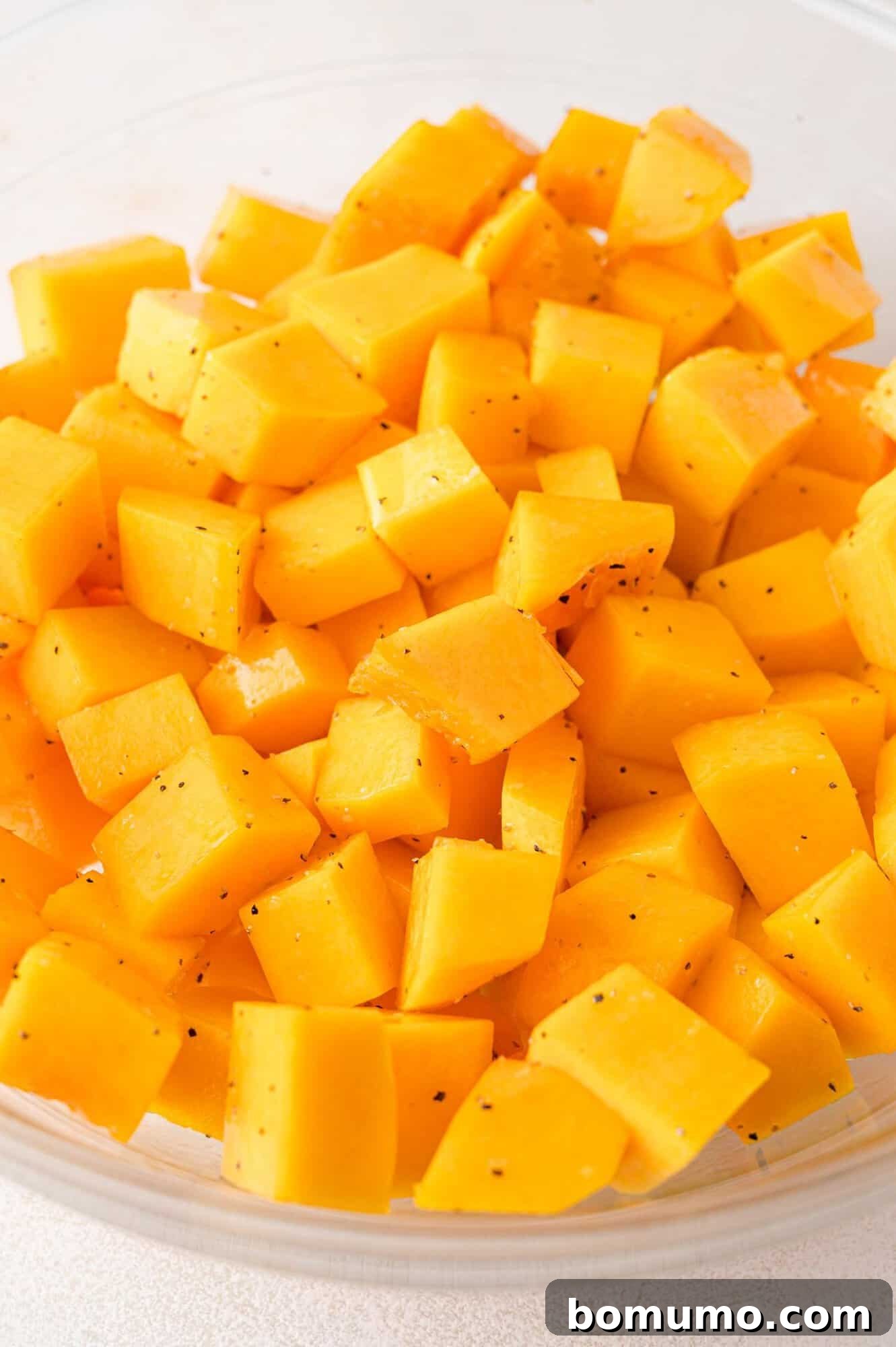 A close-up view of a vibrant bowl brimming with neatly cubed, bright orange butternut squash, showcasing its fresh and ready-to-roast state for the autumn salad.