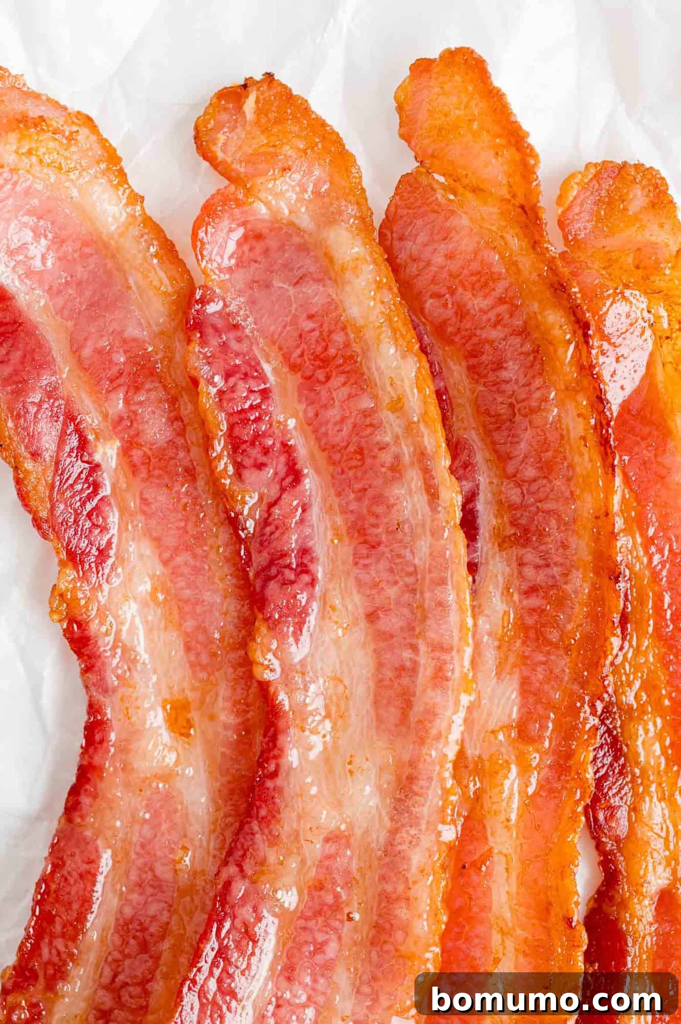 Four strips of perfectly cooked, crispy bacon rest on a clean white surface, showcasing their golden-brown color and inviting texture, ready to be crumbled into the salad.