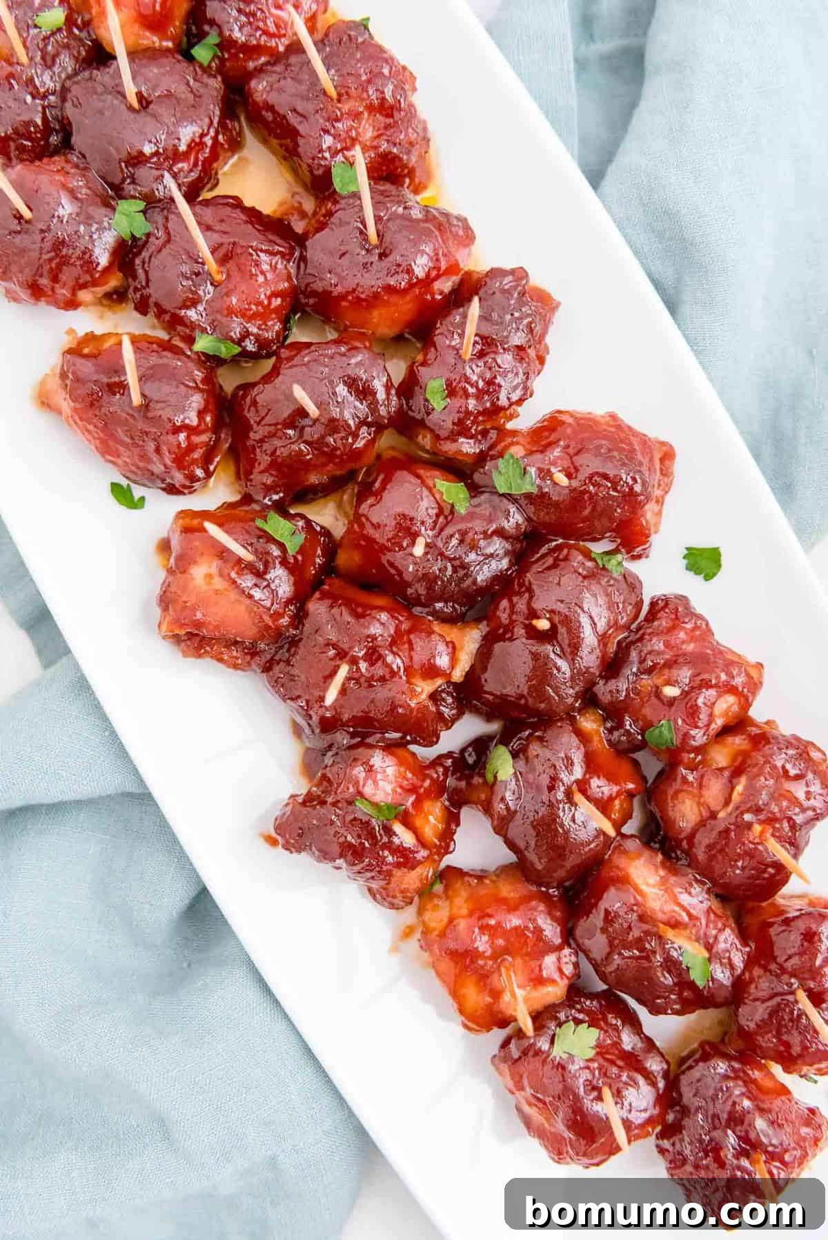 An elegant long white platter laden with rows of perfectly cooked bacon-wrapped water chestnuts, shimmering with their savory sauce, ready for guests.